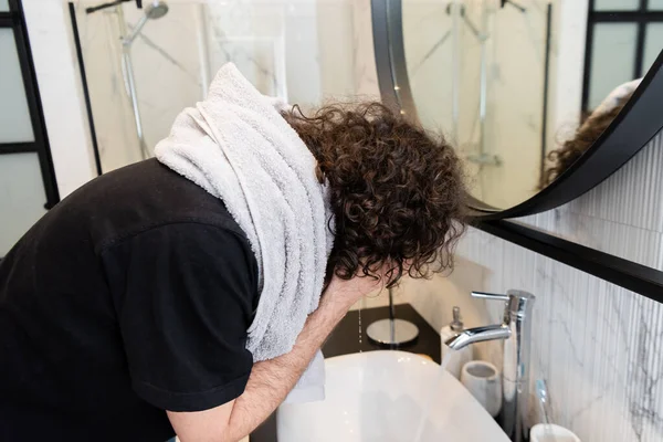 Side view of curly man washing face in bathroom — Stock Photo