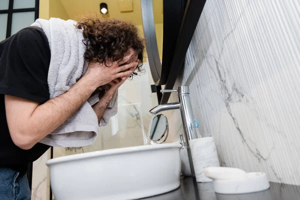 Low angle view of man with towel on shoulders washing face in bathroom — Stock Photo