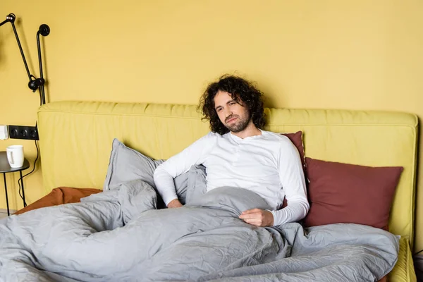 Schöner lockiger Mann sitzt zu Hause auf dem Bett — Stockfoto