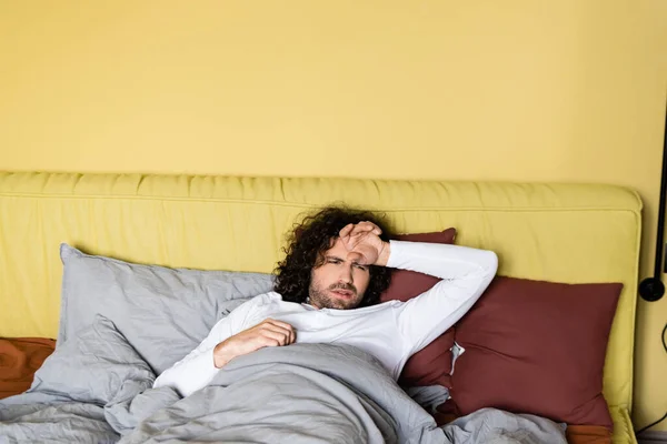 Hombre molesto con la mano cerca de la frente acostado en la cama en casa - foto de stock