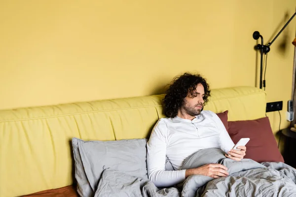 Schöner Lockenkopf mit Smartphone im Bett — Stockfoto