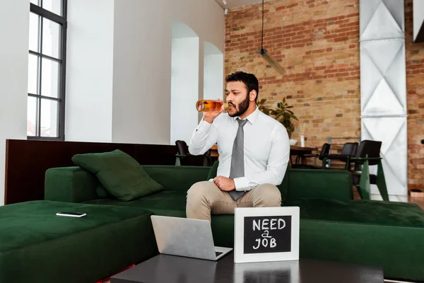 Arbeitsloser afrikanisch-amerikanischer Mann trinkt Bier in der Nähe der Tafel und braucht einen Job-Schriftzug und Laptop — Stockfoto