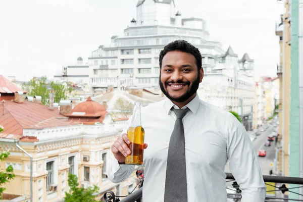 Smiling african american man holding bottle of beer on balcony — Stock Photo