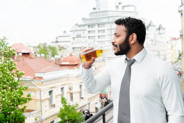 Vista laterale dell'uomo afroamericano barbuto in tuta che beve birra sul balcone — Foto stock