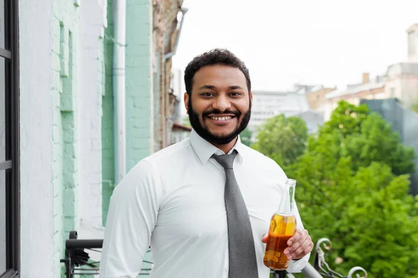 Smiling and bearded african american man holding bottle of beer on balcony — Stock Photo