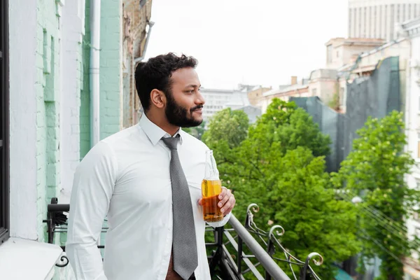 Side view of happy african american man holding bottle of beer on balcony — Stock Photo