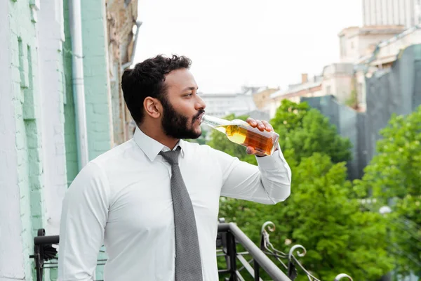 Вид збоку бородатий афроамериканський чоловік п'є пиво на балконі — стокове фото