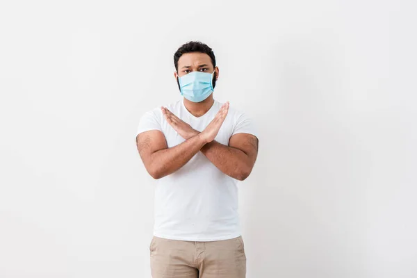 Hombre afroamericano en máscara médica mostrando señal de stop cerca de pared blanca - foto de stock