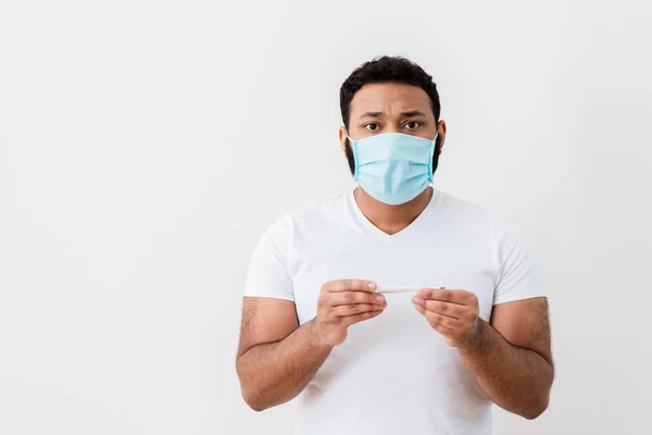 Sick african american man in medical mask holding digital thermometer near white wall — Stock Photo