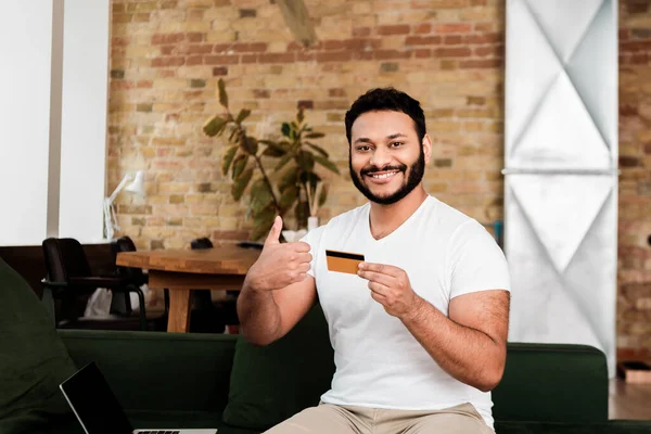 Happy african american man holding credit card near laptop with blank screen while showing thumb up — Stock Photo