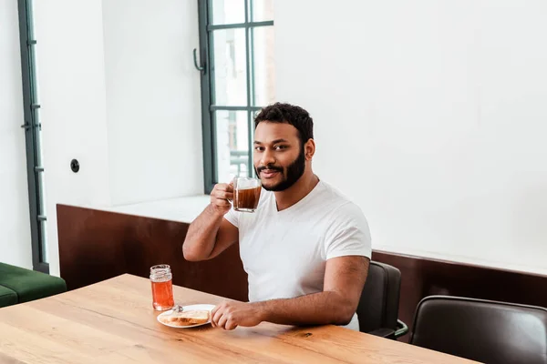 Homme afro-américain barbu tenant une tasse de café près de pain grillé avec confiture sucrée — Photo de stock