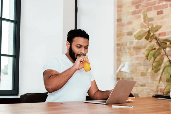 Бородатий афроамериканський фрілансер п'є апельсиновий сік під час роботи з дому — стокове фото
