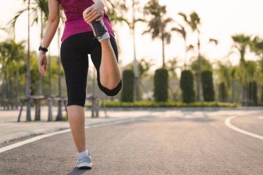 Genç bayan koşucu parkta koşmadan önce bacaklarını açıyor..