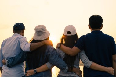 Erkek ve kadın arkadaşlarının birbirine sarılıp güneşin doğuşunu izlemesi. Mutluluk, başarı, dostluk ve toplum kavramları.