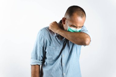 Yüz maskesi takmış bir adam, beyaz arka planda COVID-19 veya Corona virüsünün yayılmasını önlemek için dirseğine hapşırıyor ya da öksürüyor..
