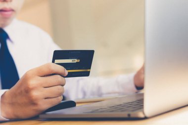 İnternetten alışveriş yapan genç bir adam internet üzerinden ödeme yapmak için kredi kartı tutuyor.