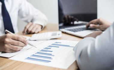 Şirketin gelir grafiğiyle ilgili iş adamları, yöneticiler ve muhasebecilerden oluşan bir ekiple ofiste dizüstü bilgisayarlar, hesap makineleri ve finans konseptiyle bir araya gelmek