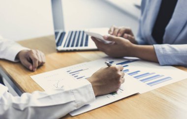 Şirketin gelir grafiğiyle ilgili iş adamları, yöneticiler ve muhasebecilerden oluşan bir ekiple ofiste dizüstü bilgisayarlar, hesap makineleri ve finans konseptiyle bir araya gelmek