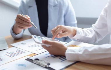 Şirketin gelir grafiğiyle ilgili iş adamları, yöneticiler ve muhasebecilerden oluşan bir ekiple ofiste dizüstü bilgisayarlar, hesap makineleri ve finans konseptiyle bir araya gelmek
