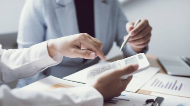 Şirketin gelir grafiğiyle ilgili iş adamları, yöneticiler ve muhasebecilerden oluşan bir ekiple ofiste dizüstü bilgisayarlar, hesap makineleri ve finans konseptiyle bir araya gelmek