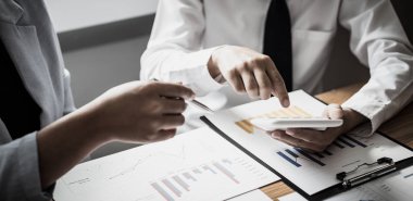 Şirketin gelir grafiğiyle ilgili iş adamları, yöneticiler ve muhasebecilerden oluşan bir ekiple ofiste dizüstü bilgisayarlar, hesap makineleri ve finans konseptiyle bir araya gelmek