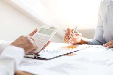 Şirketin gelir grafiğiyle ilgili iş adamları, yöneticiler ve muhasebecilerden oluşan bir ekiple ofiste dizüstü bilgisayarlar, hesap makineleri ve finans konseptiyle bir araya gelmek