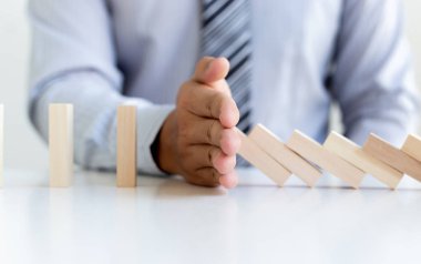 Genç adamın elleri Dominoların iş risklerini, konseptleri ve şirketleri başarı için koruma amaçlı stratejik planları azaltmak amacıyla düşmesini engelliyor.