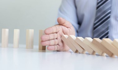 Genç adamın elleri Dominoların iş risklerini, konseptleri ve şirketleri başarı için koruma amaçlı stratejik planları azaltmak amacıyla düşmesini engelliyor.