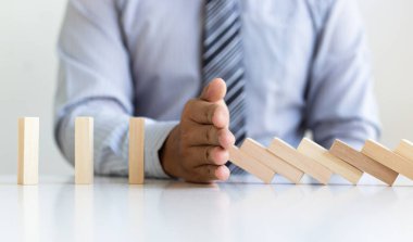 Genç adamın elleri Dominoların iş risklerini, konseptleri ve şirketleri başarı için koruma amaçlı stratejik planları azaltmak amacıyla düşmesini engelliyor.