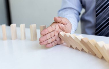 Genç adamın elleri Dominoların iş risklerini, konseptleri ve şirketleri başarı için koruma amaçlı stratejik planları azaltmak amacıyla düşmesini engelliyor.