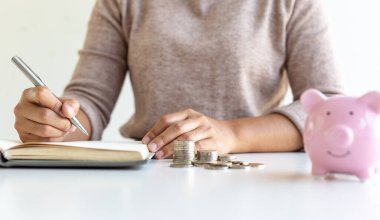 Genç iş kadınları, emlak, vergi indirimi ve maliyet hesaplama konseptine yatırım hazırlamak için bir domuz kumbarasında para biriktiriyorlar ve mali gelir harcamalarını kaydediyorlar..