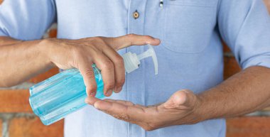 Genç adam ellerini mavi alkolle yıkıyordu. Temizlik için colona virüsünü öldürmek ve COVID-19 'un tüm dünyaya yayılmasını engellemek için. Hijyen ve temizlik kavramları..