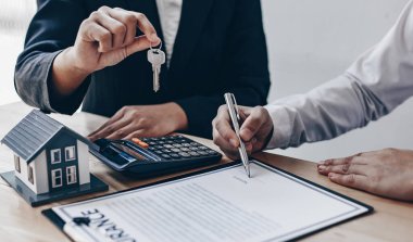 Emlakçı müşteriye gönderilecek anahtarları elinde tutuyor ve ev satışı anlaşmasını ve ev sigortasını müşteriye, ev satışları ve ev sigortası kavramına imzalama şartlarını sunuyor..