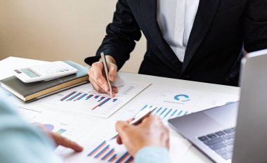 Şirketin gelir grafiğiyle ilgili iş adamları, yöneticiler ve muhasebecilerden oluşan bir ekiple ofiste dizüstü bilgisayarlar, hesap makineleri ve finans konseptiyle bir araya gelmek.
