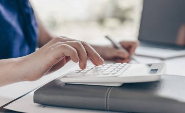 Muhasebe işadamları gelir-gider hesapları yapıyor ve gayrimenkul yatırım verilerini analiz ediyor, o bir masanın üzerinde çalışıyor dizüstü bilgisayarlı grafikler ve hesap makineleri, mali ve vergi sistemleri kavramları var.