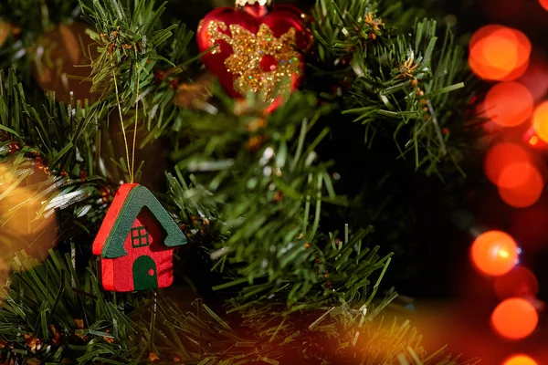 Christmas tree toy house on the tree hanging on the background of green needles and Christmas tree toys red heart and colorful bokeh