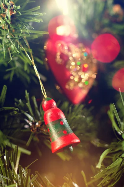 Ağaçta asılı Noel ağacı çanı yeşil iğneler ve Noel ağacı oyuncakları kırmızı kalp ve renkli bokeh