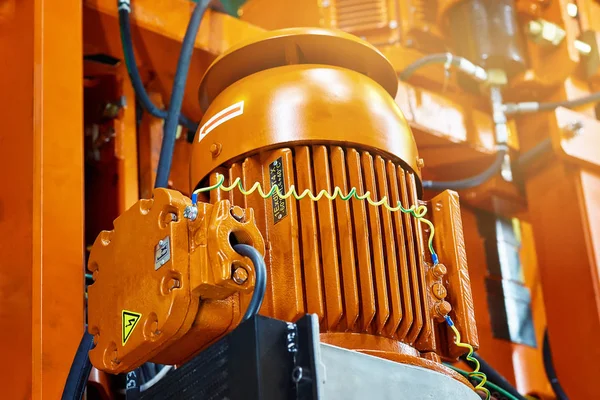 Electric motor orange with wires and hoses on the background of heavy engineering construction