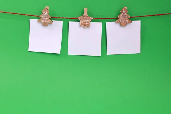 A garland of white empty leaves hanging on a rope on wooden clothespins with Christmas theme on a green background. Christmas decoration. Copy space. Blank paper cards hanging on clothespins.