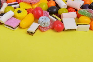 Set with various colorful candies on a yellow background, top view. Close up of mixed sweets. Space for text.