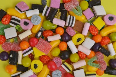 Set with various colorful candies on a yellow background, top view. Close up of mixed sweets. Space for text.