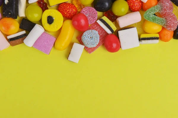 Set with various colorful candies on a yellow background, top view. Close up of mixed sweets. Space for text.