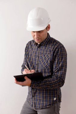 Miğferli genç müteahhit, iş planına bakıyor. Metin alanı olan beyaz bir arkaplanda izole edilmiş.