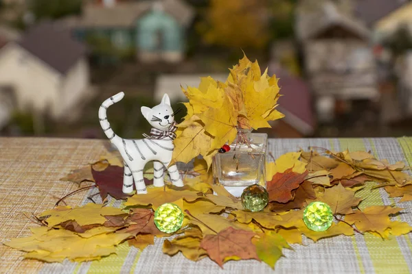 still life with maple, leaves, in a glass, small, vase, large, green, beads and a statuette of a white clay cat