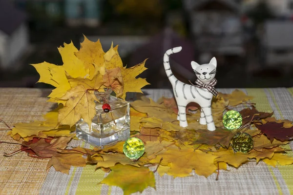still life with maple, leaves, in a glass, small, vase, round, green, beads and a statuette of a white clay cat