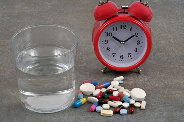 Sleeping pills next to a glass of water and an alarm clock