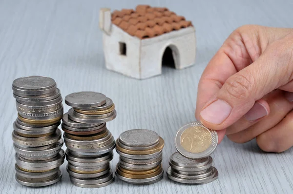 Hand stacking coins with a house in the background