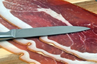 Slices of Aosta ham on a cutting board close-up with a knife 