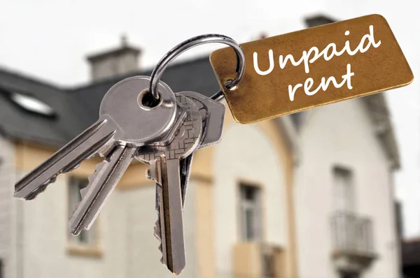 Concept of unpaid rent with a bunch of keys in close up and a house in the background 
