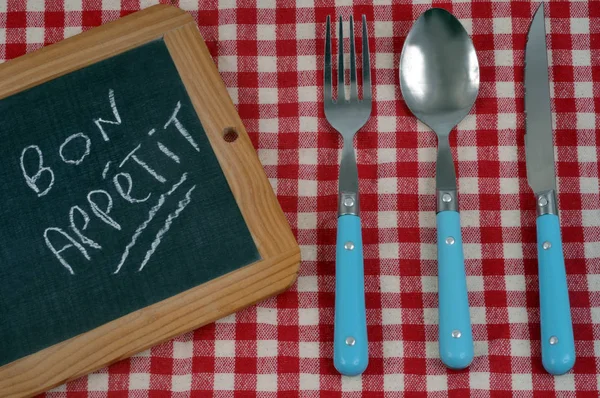 Bon appetit written on a school slate placed on a table next to cutlery